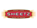 Sheetz logo featuring the word 'Sheetz' in bold, white, stylized letters on a red rectangular background with a yellow border. Above it says 'fresh food' and below it says 'made to over' over two more red rectangles. On the left and right are gold lines fanning out.